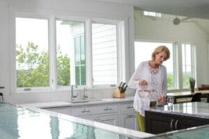 A woman pours a glass of water in front of large windows in a kitchen