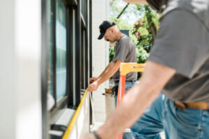 Two workers measure a window for bullet-resistant glass installation.